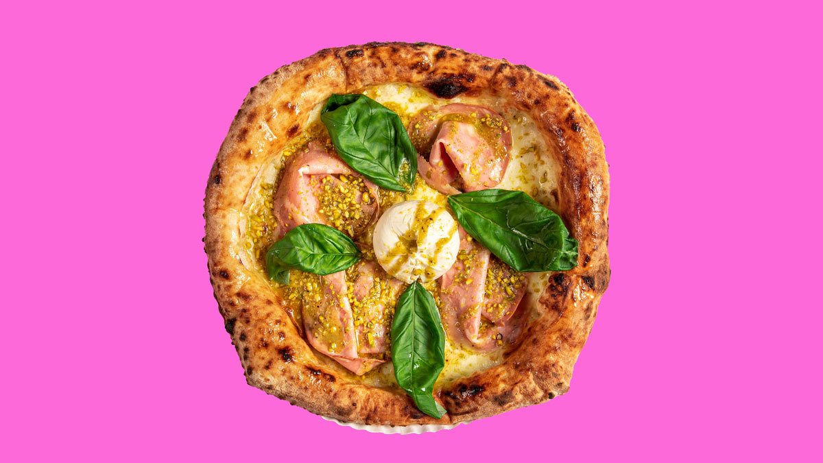 Pizza mit Schinken, Basilikum und Mozzarella auf pinkem Hintergrund; knuspriger Rand.
