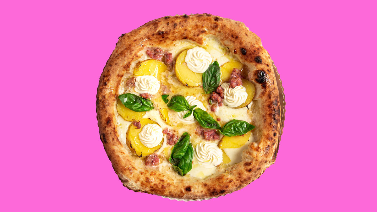 Pizza mit gelben Tomaten, Wurst, Basilikum und Sahne auf pinkem Hintergrund.